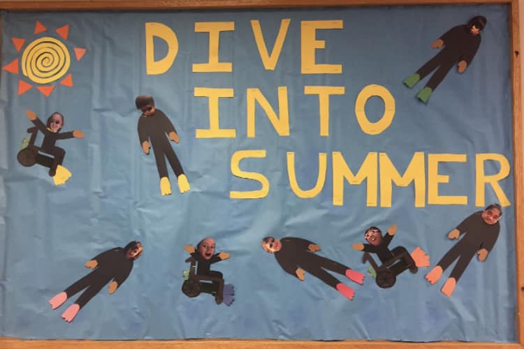 A bulletin board says Dive Into Summer and features little divers with students' faces on them.