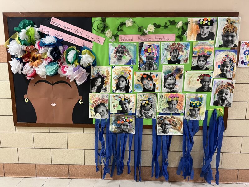 A bulletin board features a head with flowers on it and pictures of all the students in the class. It says Famous Artists Frida Kahlo.