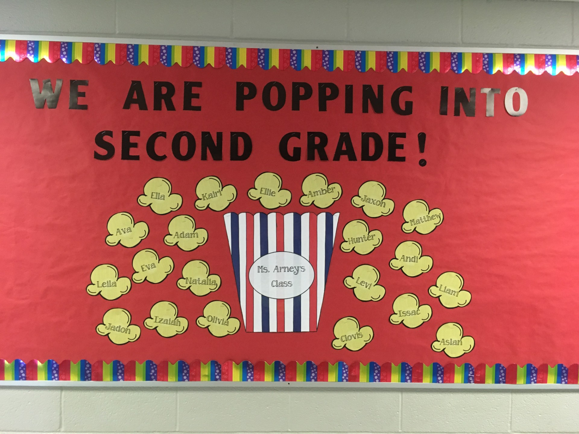 A bulletin board says We Are Popping Into Second Grade. Popcorn kernels have students' names on them.