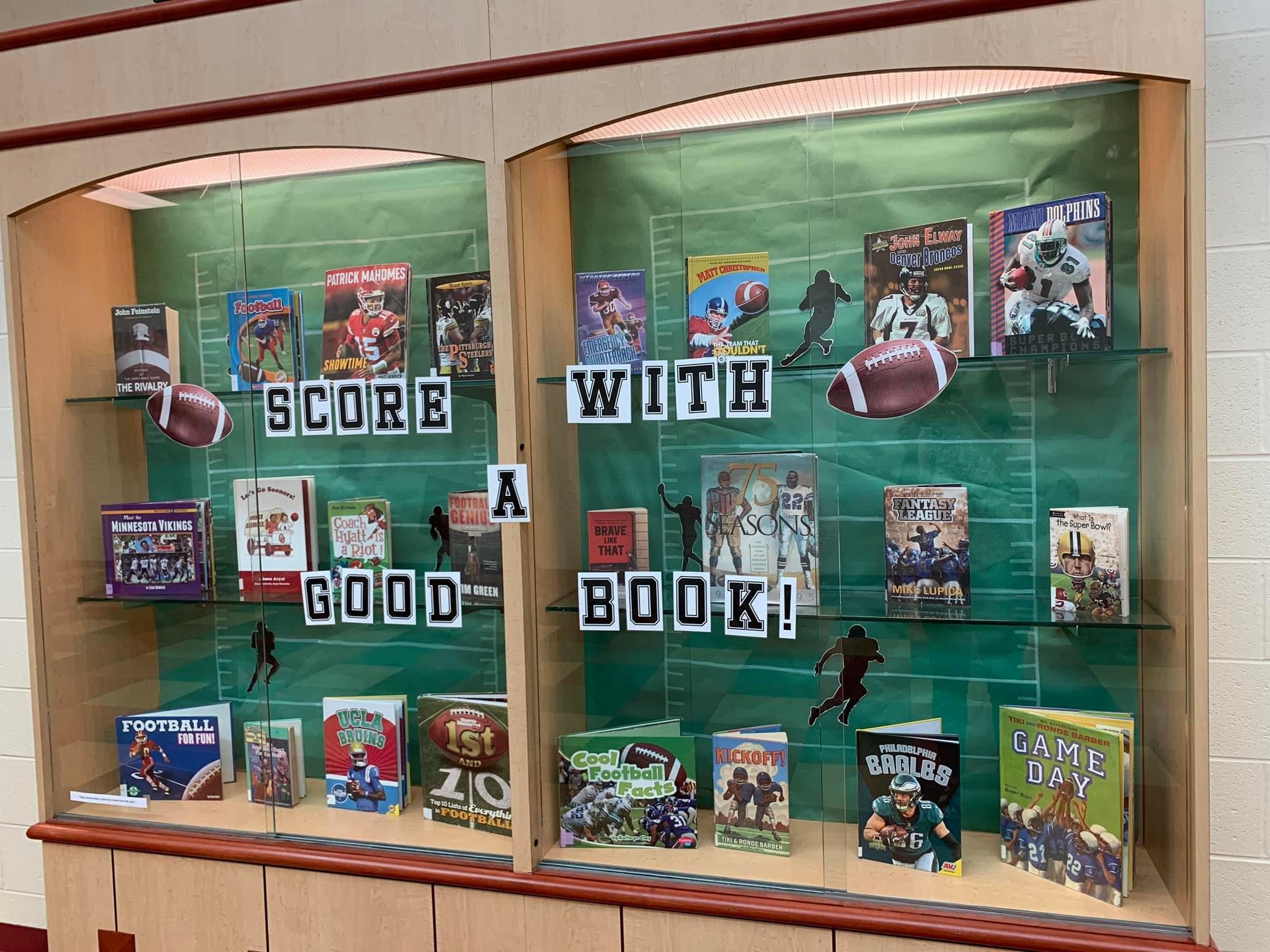 A display case cover says Score with a Good Book and has a bunch of football books