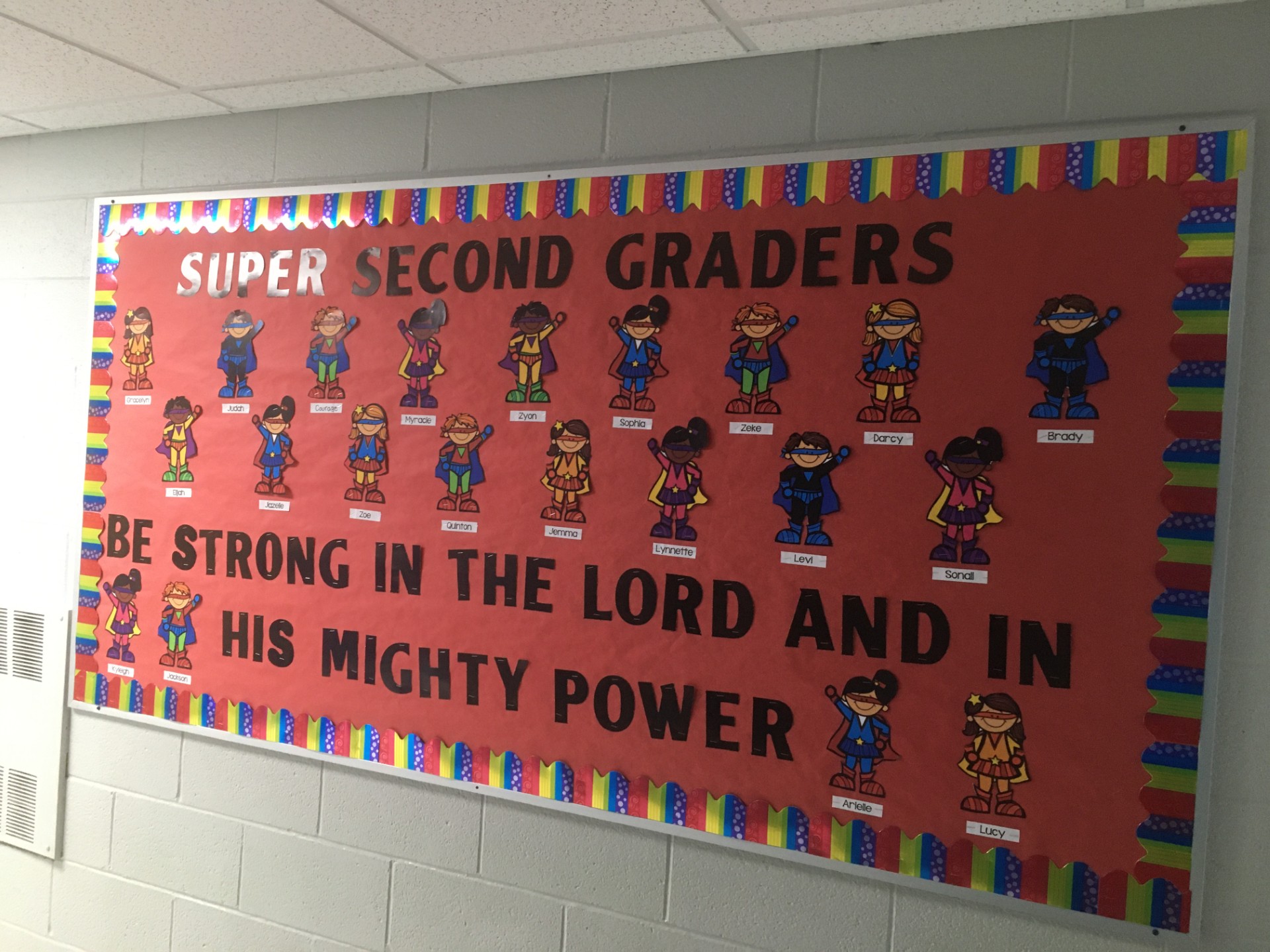 A bulletin board features little superheroes with student names on them.
