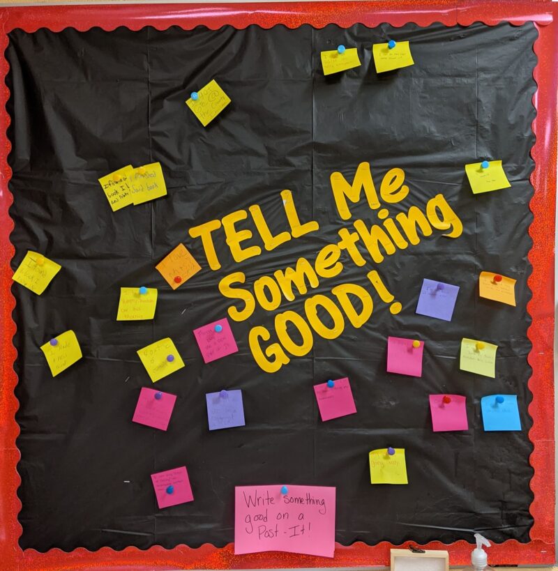 A bulletin board with a black background reads Tell Me Something Good. Sticky notes are attached with good news from students about their week.