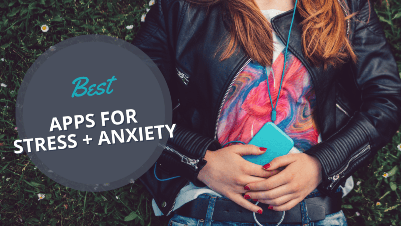 Teen girl laying on grass listening to best apps for anxiety and stress on headphones using smart phone.