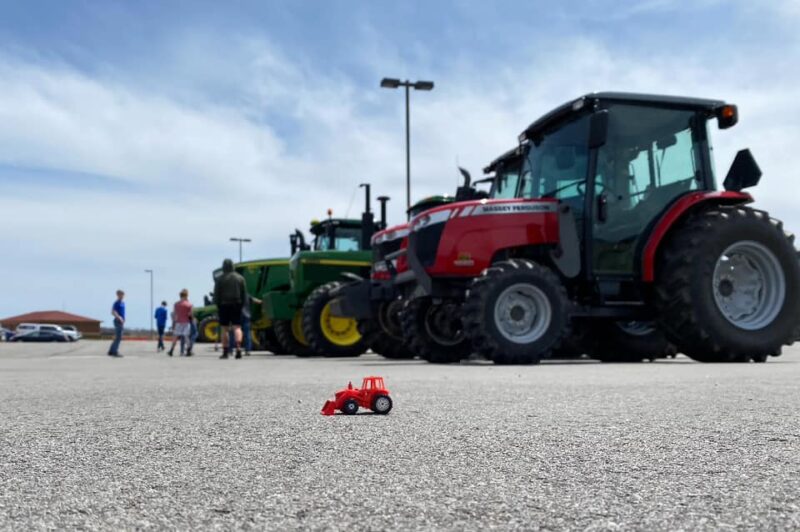 Tractors in a parking lot with a small tractor in front 