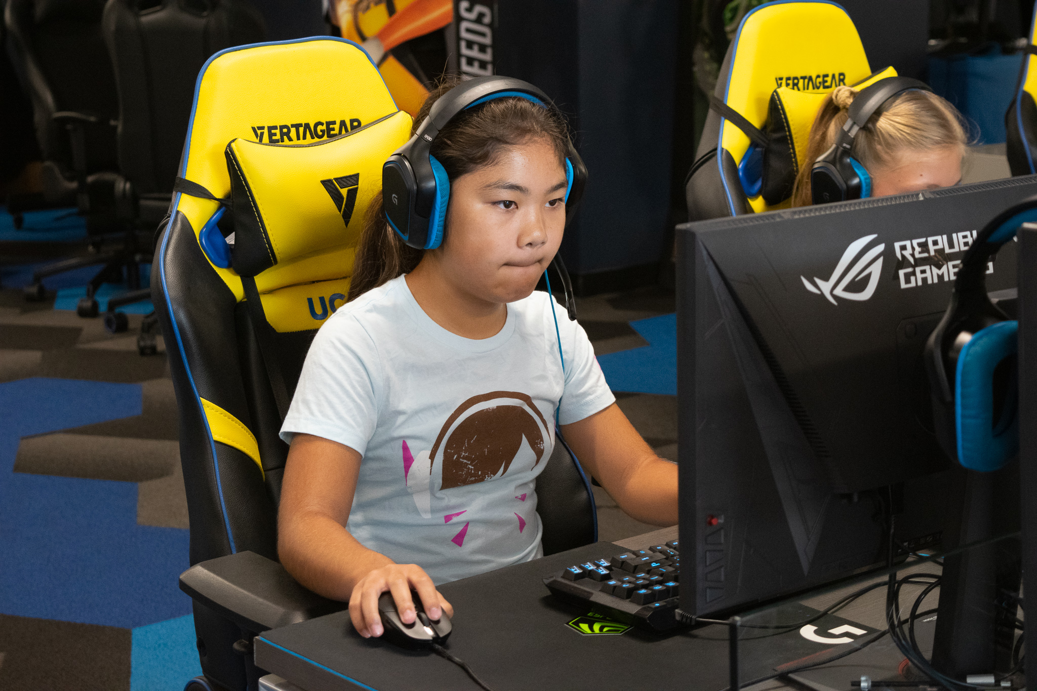 A young girls wearing a headset sits in front of a computer screen playing esports.