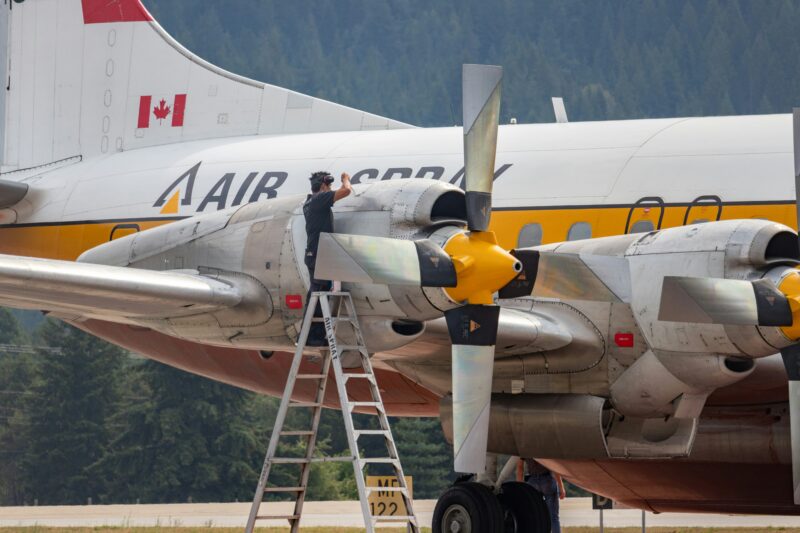 An airplane technician (one of the best jobs without a college degree) stands on a ladder fixing a plane propellor.- best jobs without a college degree