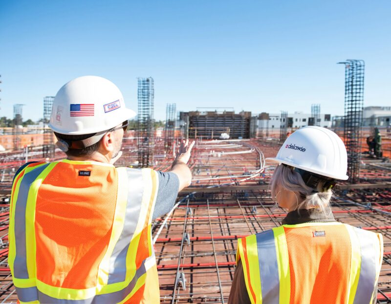 Two workers wearing orange safety vests and hard hats stand looking out over a loading area. One is a construction manager, one of the best jobs without a college degree.