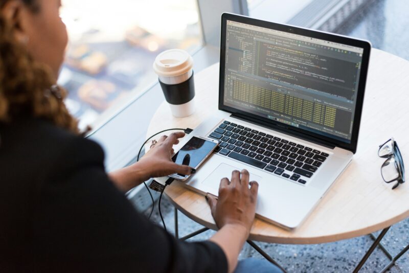 A mobile app developer works at a laptop with a smartphone nearby